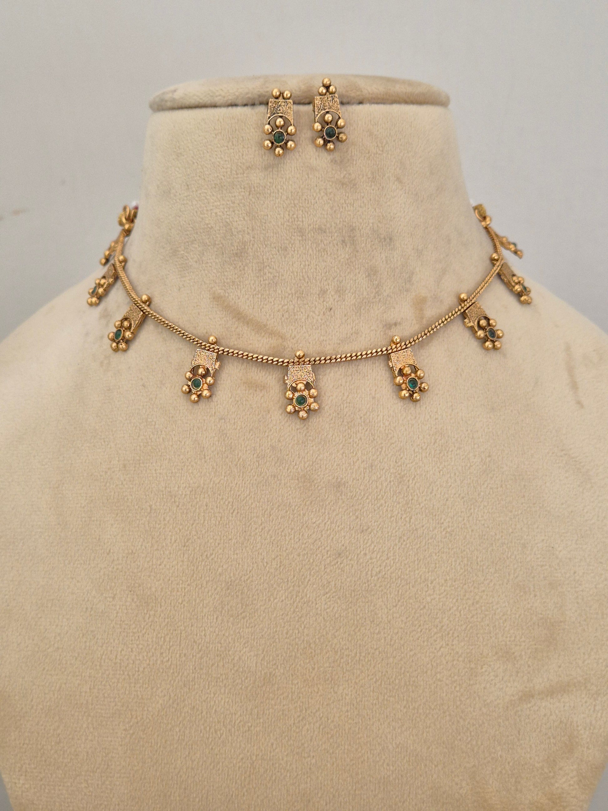 Traditional Indian gold-toned choker necklace with delicate hanging floral charms accented with green gemstones by naitri.in