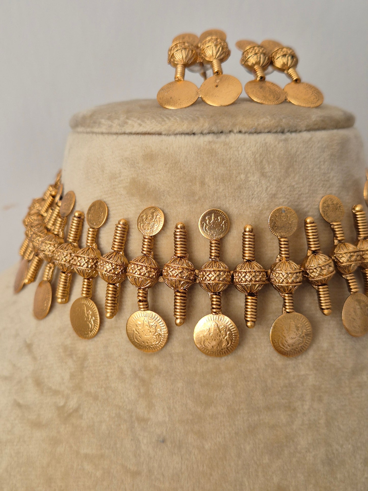Traditional Indian coin choker necklace set with an antique gold finish, intricately textured metal stamping, and a structured collar silhouette from the Naitri Golden Ethnic Jewellery collection by naitri.in