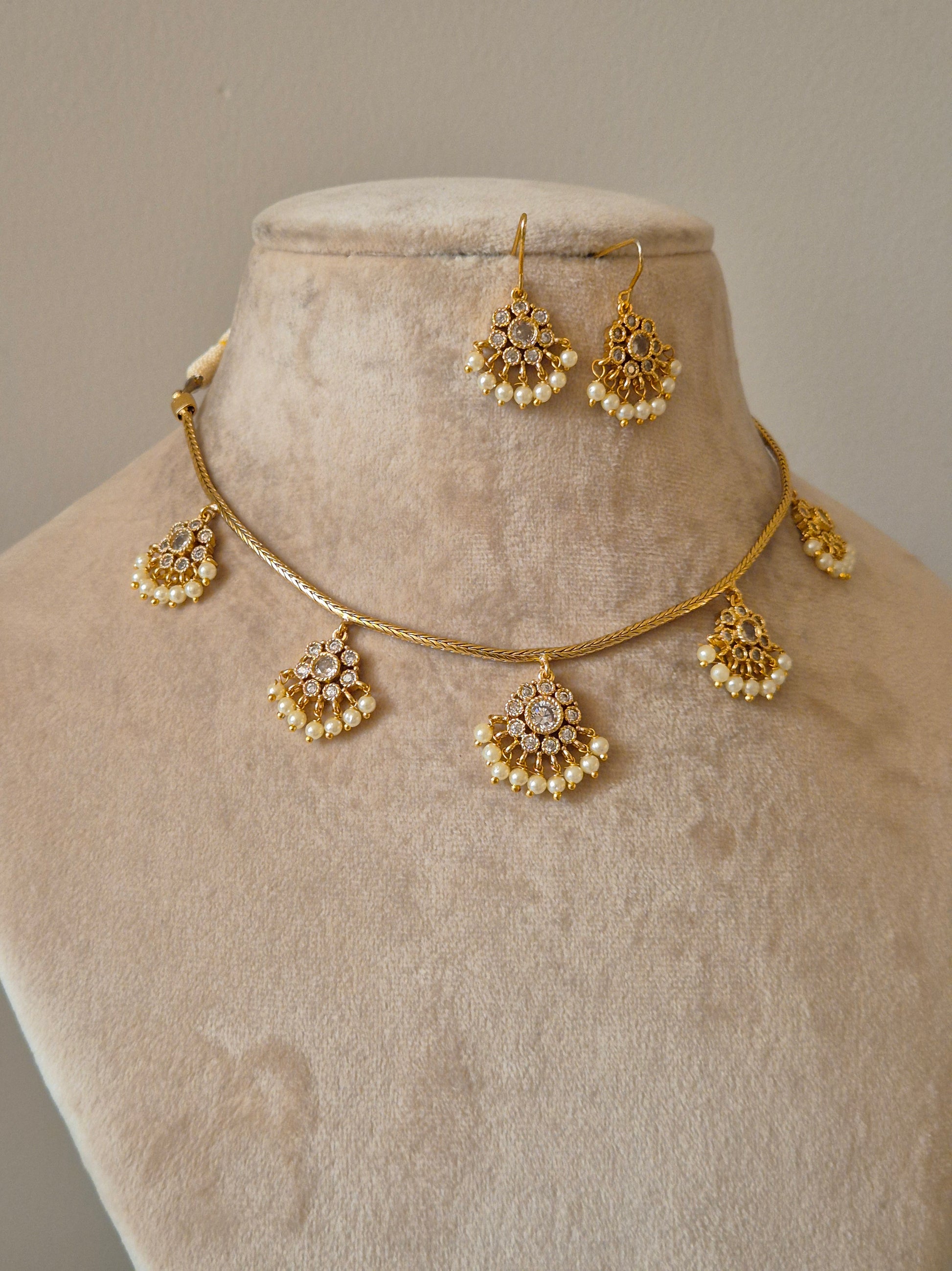 Minimalist gold-tone brass necklace featuring intricate arched pendants with white stone embellishments and small pearl dangles, paired with matching stud earrings by naitir.in
