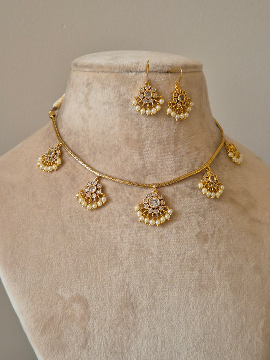 Minimalist gold-tone brass necklace featuring intricate arched pendants with white stone embellishments and small pearl dangles, paired with matching stud earrings by naitir.in