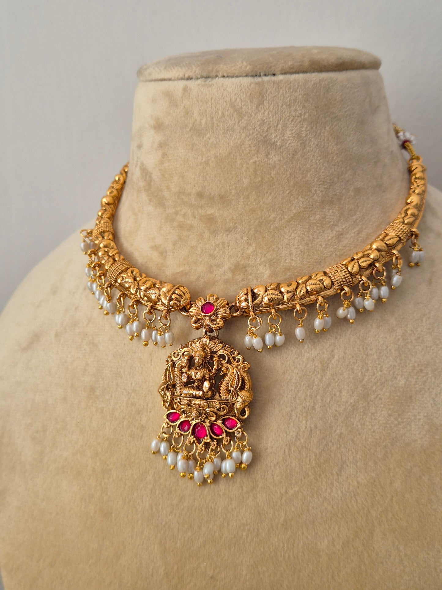 Traditional Indian antique-finish brass necklace set showcasing intricate floral metalwork, a deity-engraved central pendant, and rich white pearl cluster fringes from the Naitri Golden Ethnic Jewellery collection by naitri.in