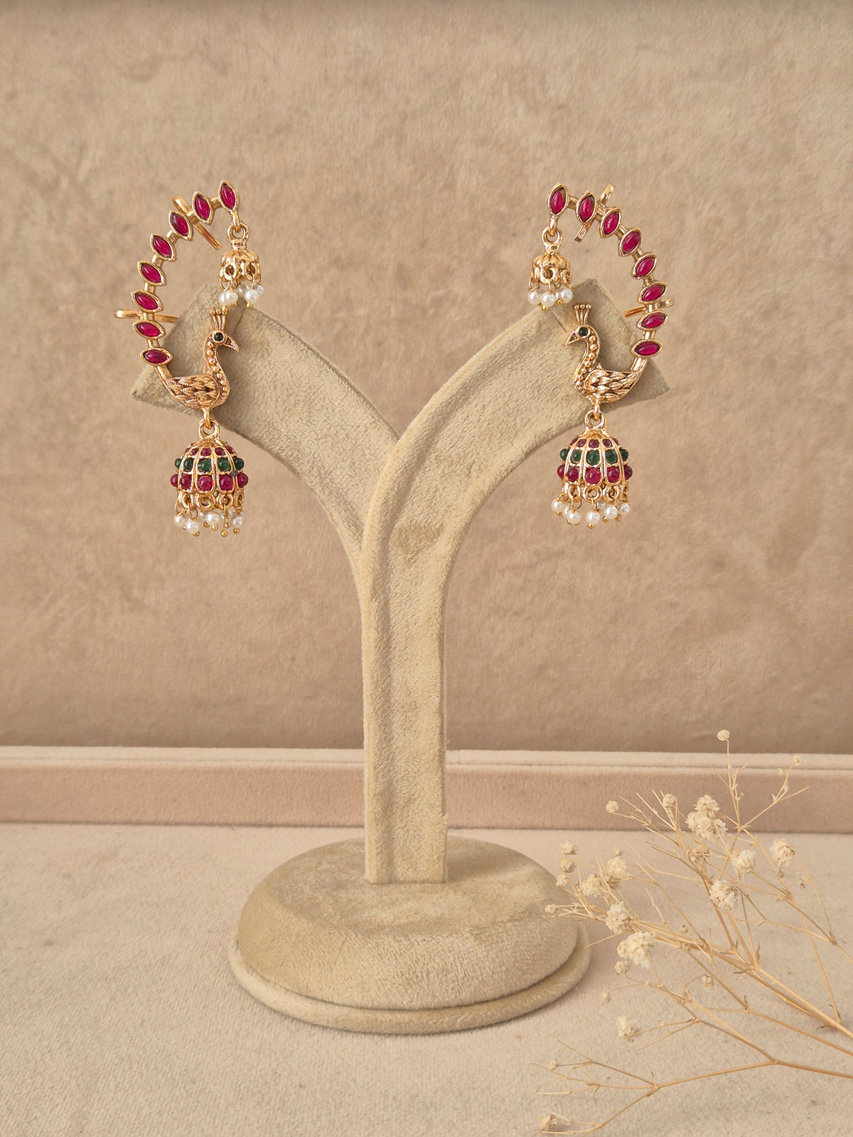 Gold-plated peacock jhumka earrings featuring a curved hoop studded with ruby-red stones leading to a bell-shaped dome with pearl drops by naitri.in