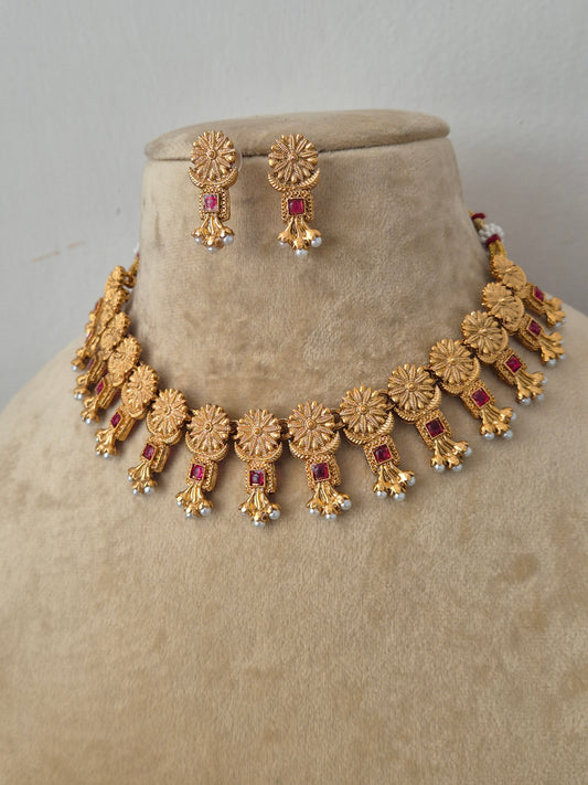Gold-plated ethnic choker set featuring intricate textured circular engravings, small red stone embellishments, and delicate white hanging pearls by naitri.in