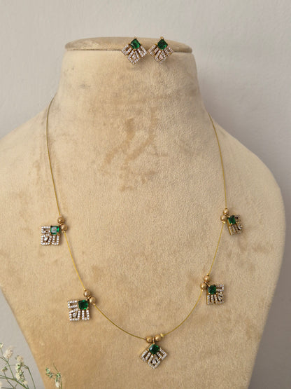 Minimalist gold-toned fine chain necklace featuring five evenly spaced, fan-shaped geometric charms accented with emerald-green gemstones and clear crystals, shown with matching stud earrings by naitri.in