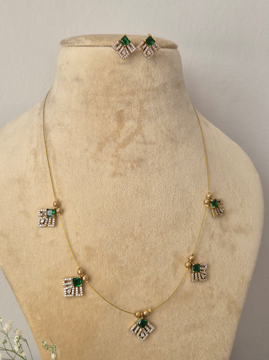 Minimalist gold-toned fine chain necklace featuring five evenly spaced, fan-shaped geometric charms accented with emerald-green gemstones and clear crystals, shown with matching stud earrings by naitri.in