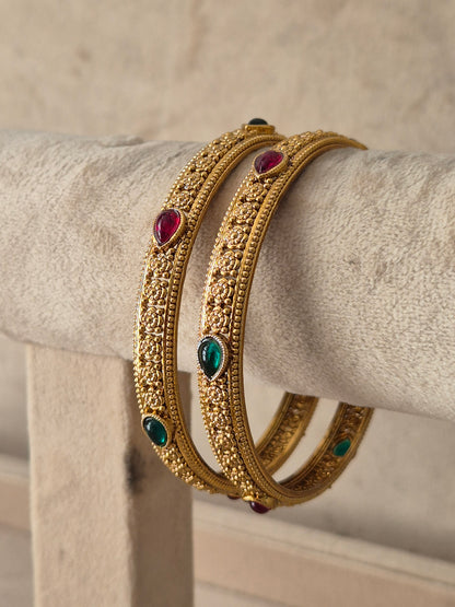 A pair of gold-plated bangles with intricate filigree detailing and small colorful gemstone accents, by naitri.in