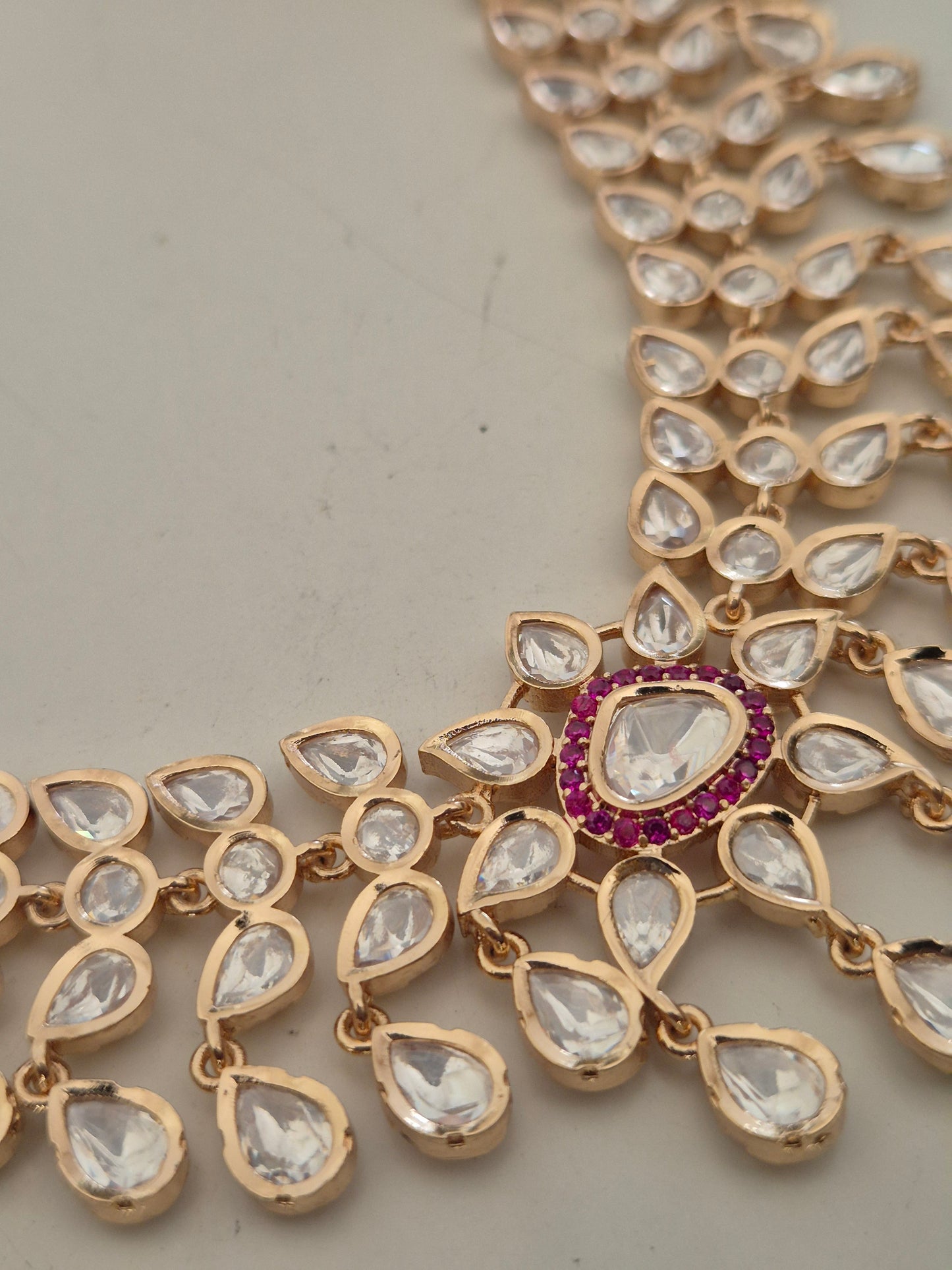 Rose-Gold toned alloy necklace with a multi-layered American Diamond design, ruby-red stones side of big clear AD stone by naitri.in