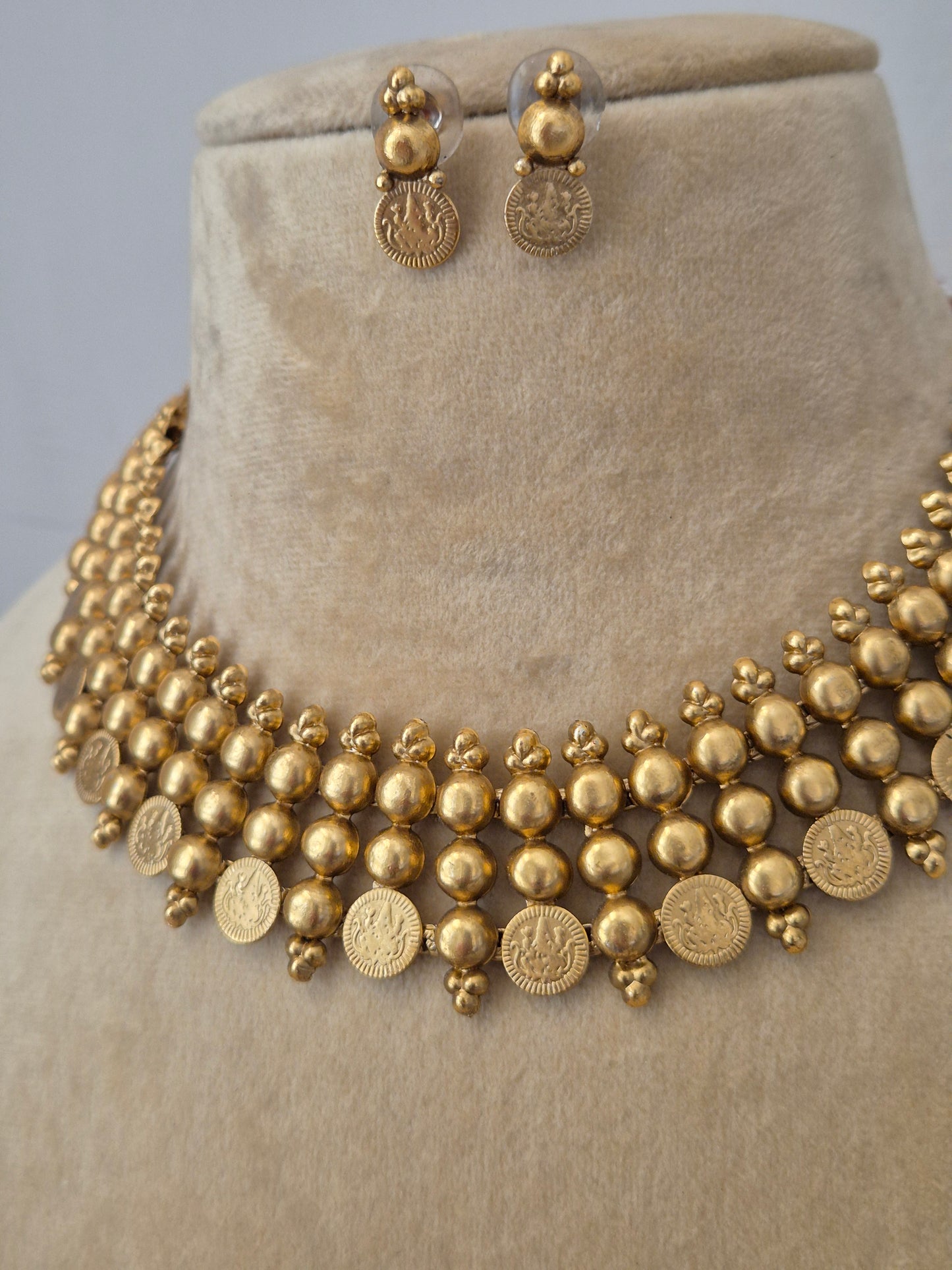 Traditional Indian temple-style gold necklace featuring multi-layered gold beads and hanging coin charms, shown with matching small drop earrings by naitri.in