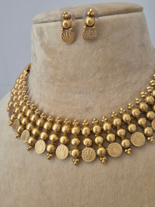 Traditional Indian temple-style gold necklace featuring multi-layered gold beads and hanging coin charms, shown with matching small drop earrings by naitri.in