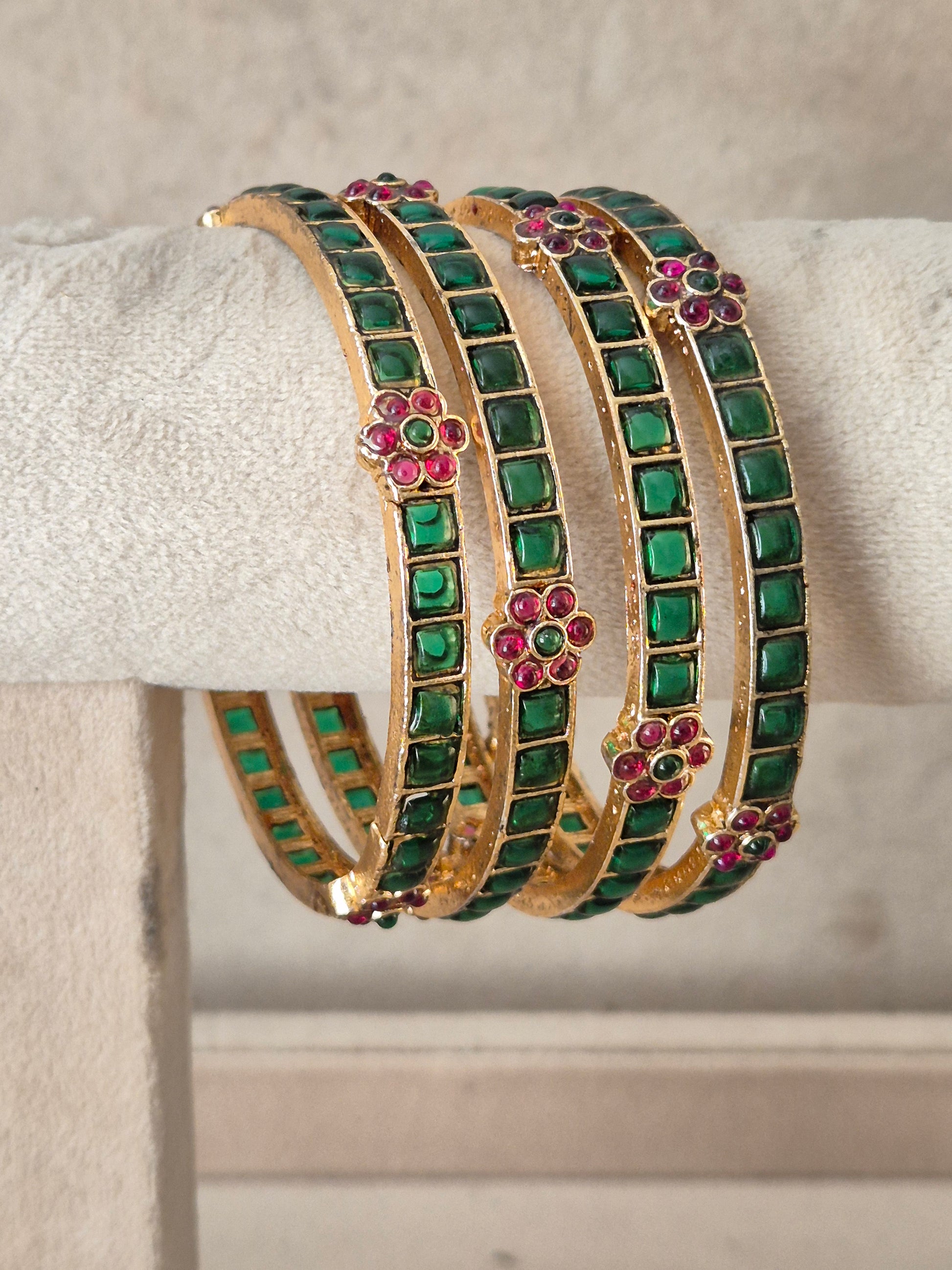 A stack of four gold-toned bangles decorated with rows of green square stones and small pink floral accents, by naitri.in .