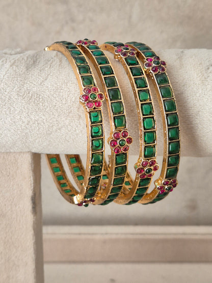 A stack of four gold-toned bangles decorated with rows of green square stones and small pink floral accents, by naitri.in .