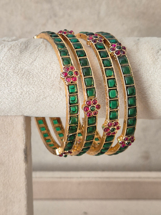A stack of four gold-toned bangles decorated with rows of green square stones and small pink floral accents, by naitri.in .