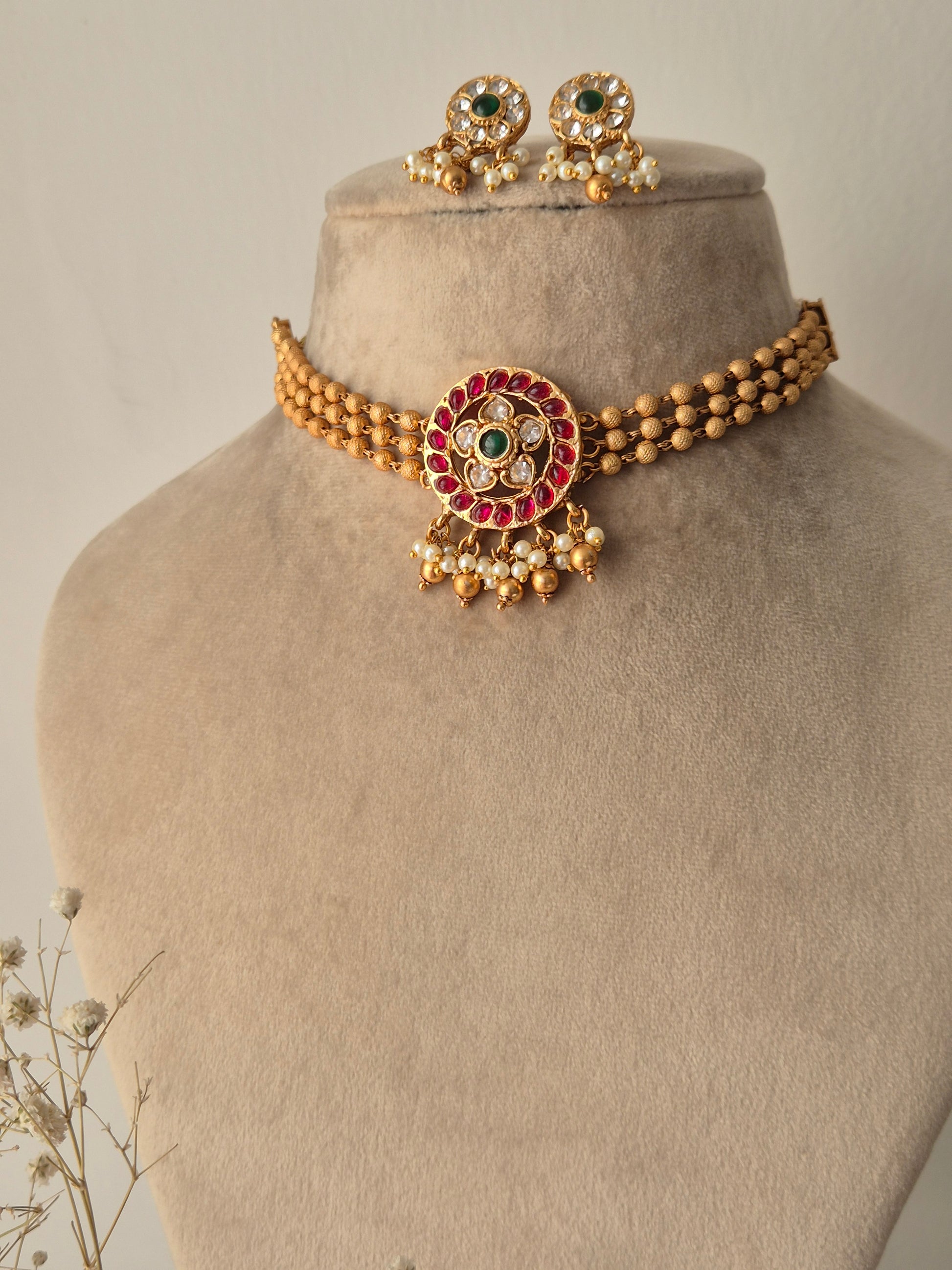 Gold bracelet with red, green and clear stones, gold beaded 3-layered chain for choker, some pearls and golden beads hanging from the pendant same designed earrings flora design choker set by naitri.in