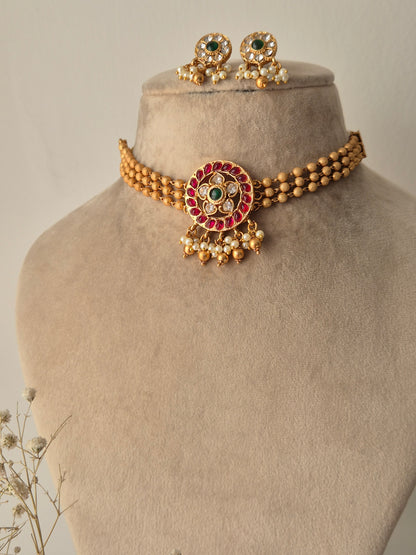 Gold bracelet with red, green and clear stones, gold beaded 3-layered chain for choker, some pearls and golden beads hanging from the pendant same designed earrings flora design choker set by naitri.in