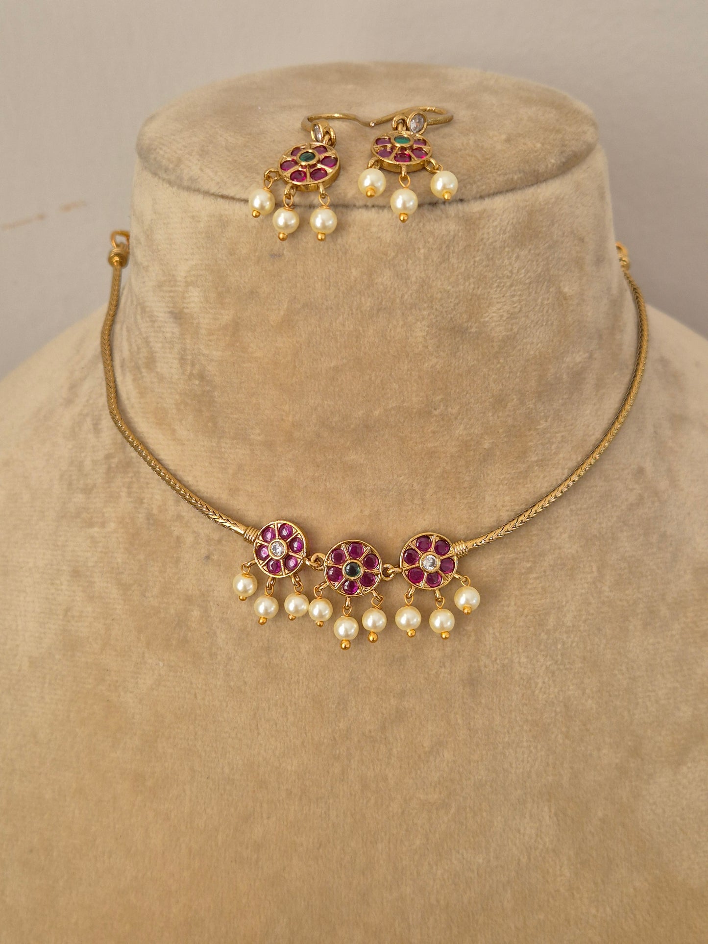 Traditional Indian antique-finish brass jewelry set showcasing a minimalist gold strand choker adorned with vibrant pink and green floral stone motifs and hanging pearl fringes from the Naitri collection by naitri.in