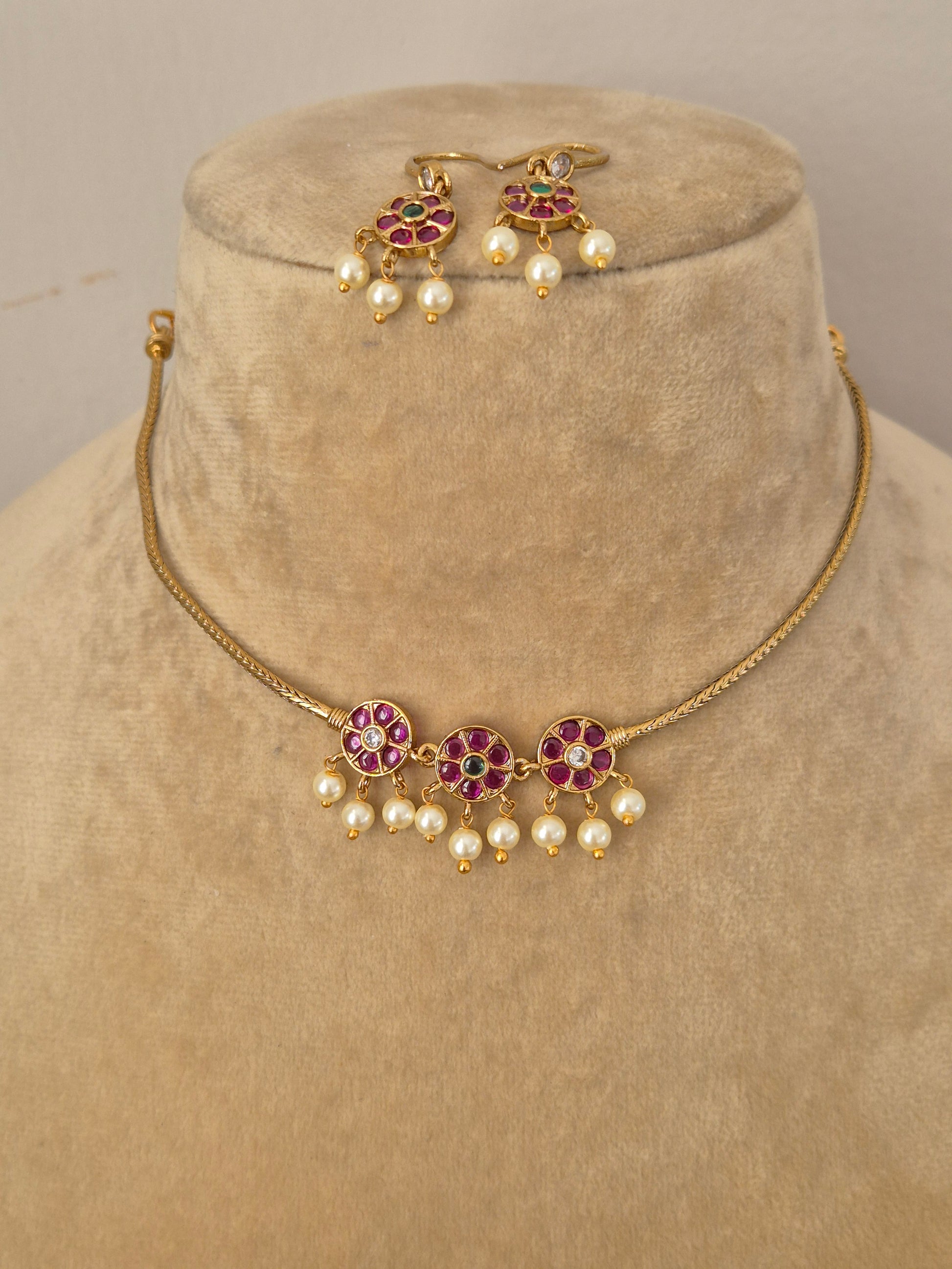 Traditional Indian antique-finish brass jewelry set showcasing a minimalist gold strand choker adorned with vibrant pink and green floral stone motifs and hanging pearl fringes from the Naitri collection by naitri.in