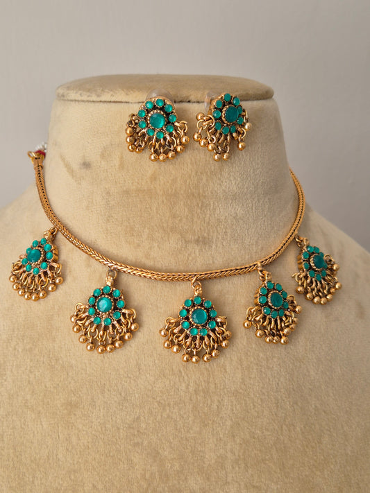 Traditional gold and turquoise necklace set with a classic design, displayed on a beige mannequin bust with delicate dried flowers for a modern Indian aesthetic by naitri.in