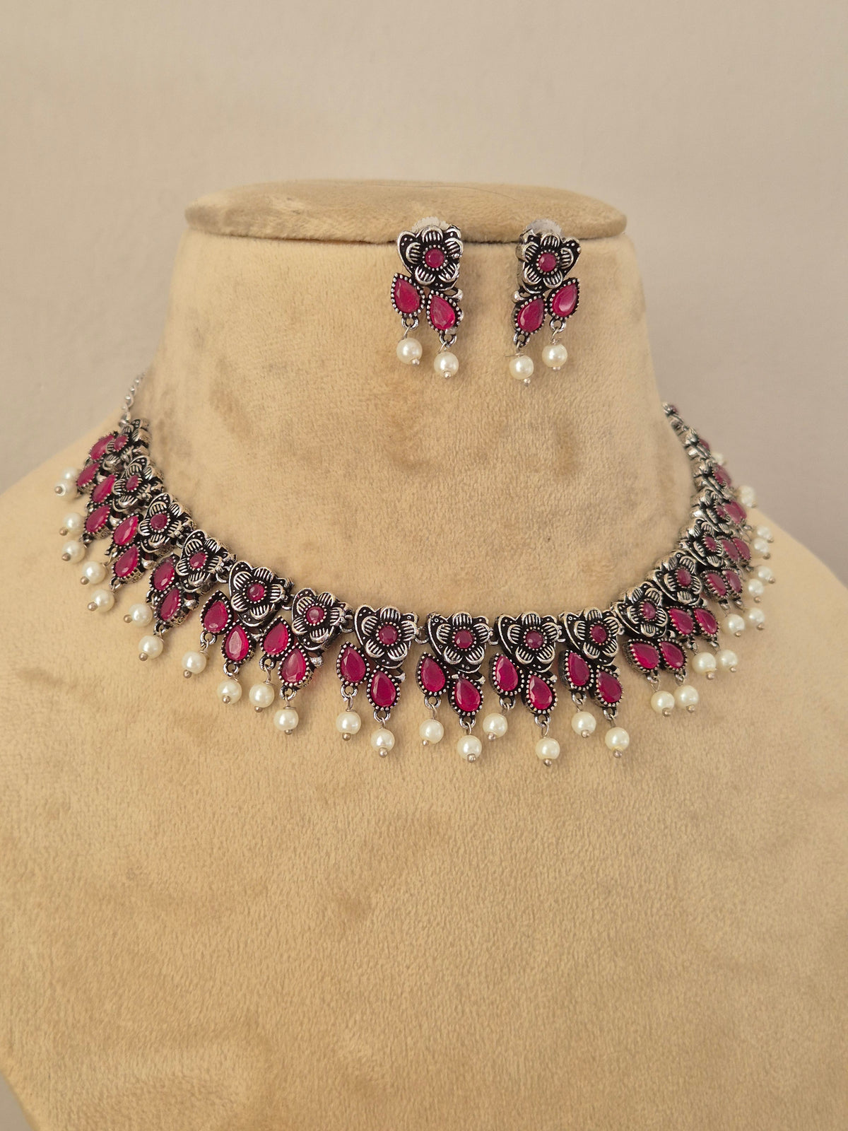 Pair of oxidized silver floral motif choker necklace with matching red stone earrings  by Naitri.in