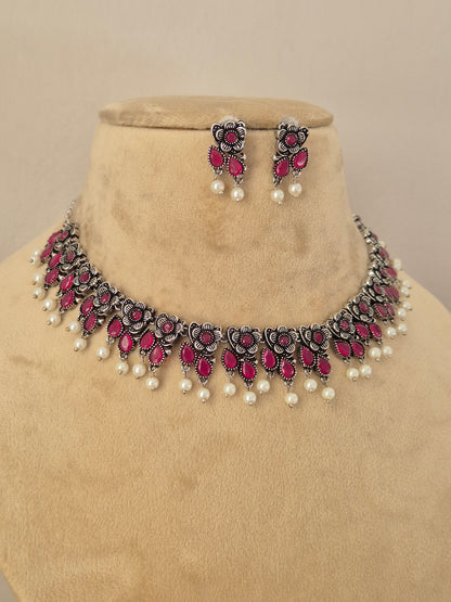 Pair of oxidized silver floral motif choker necklace with matching red stone earrings  by Naitri.in