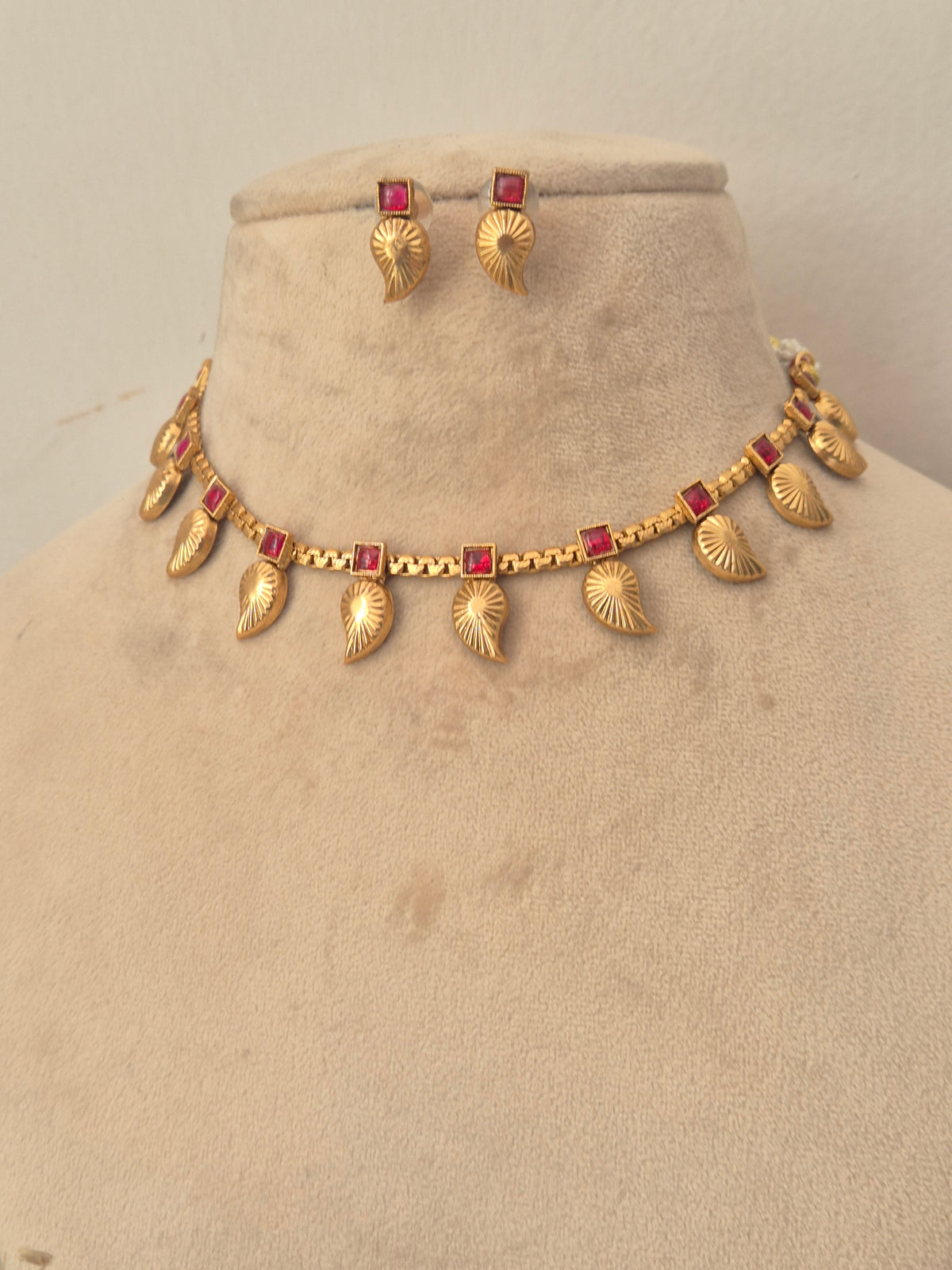 Gold leaf-pattern choker necklace with red stone accents and matching earrings by naitri.in
