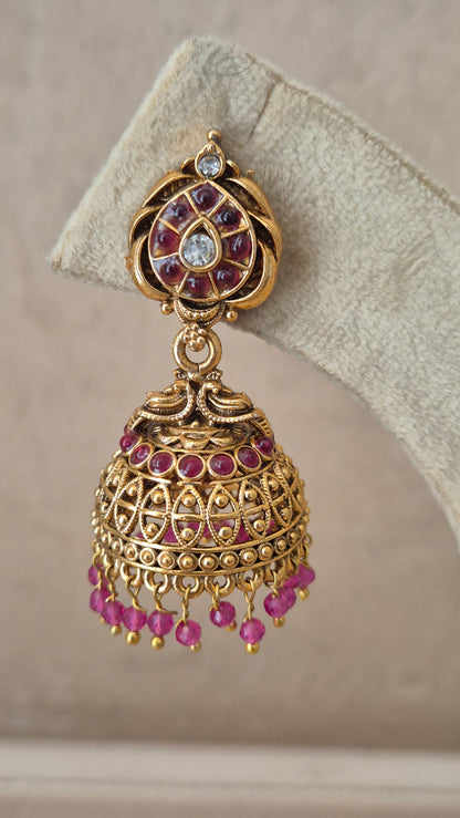 Close-up of Naitri Urjita premium gold ethnic earrings showcasing traditional Indian temple jewelry craftsmanship with vibrant ruby pink gemstone accents. by naitri.in