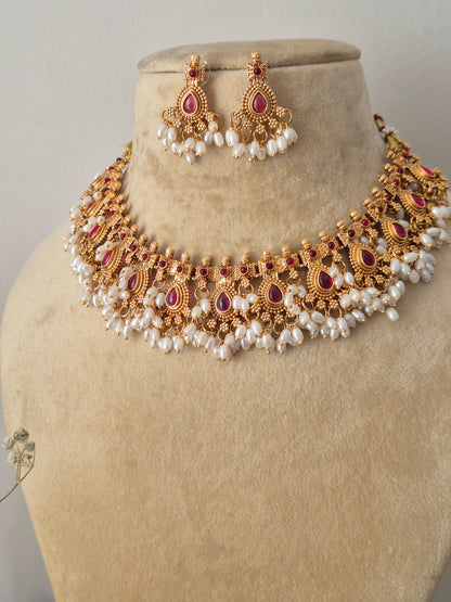 Traditional Indian antique-finish brass jewelry set showcasing a structured collar necklace with ruby-pink gemstone embellishments and dangling seed pearls from the Naitri collection by naitri.in