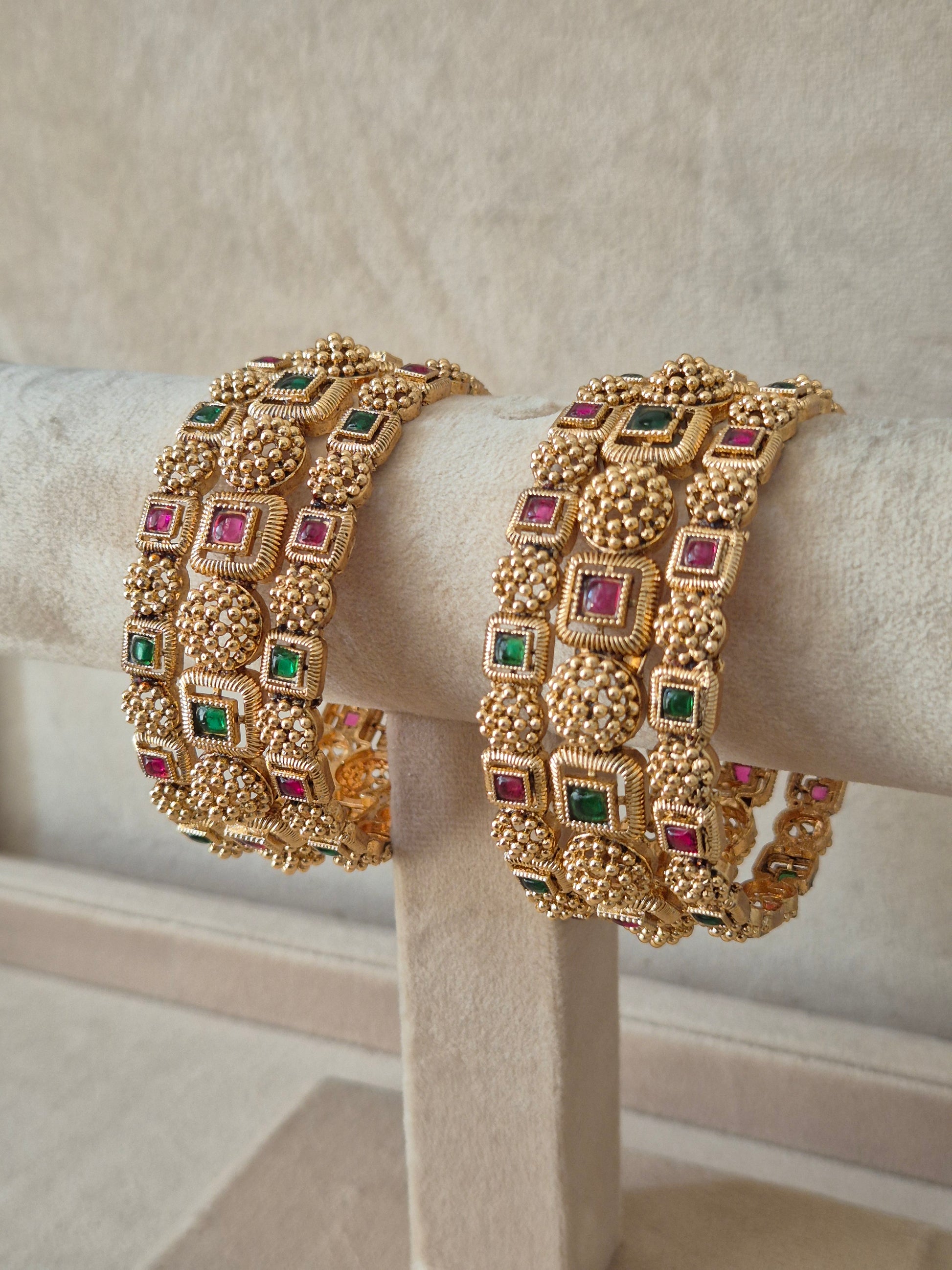 Close-up of Naitri Uttura premium gold ethnic bangle set with traditional Indian floral metalwork and vibrant red and green stone accents. by naitri.in