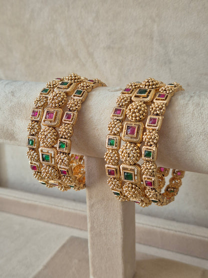 Close-up of Naitri Uttura premium gold ethnic bangle set with traditional Indian floral metalwork and vibrant red and green stone accents. by naitri.in