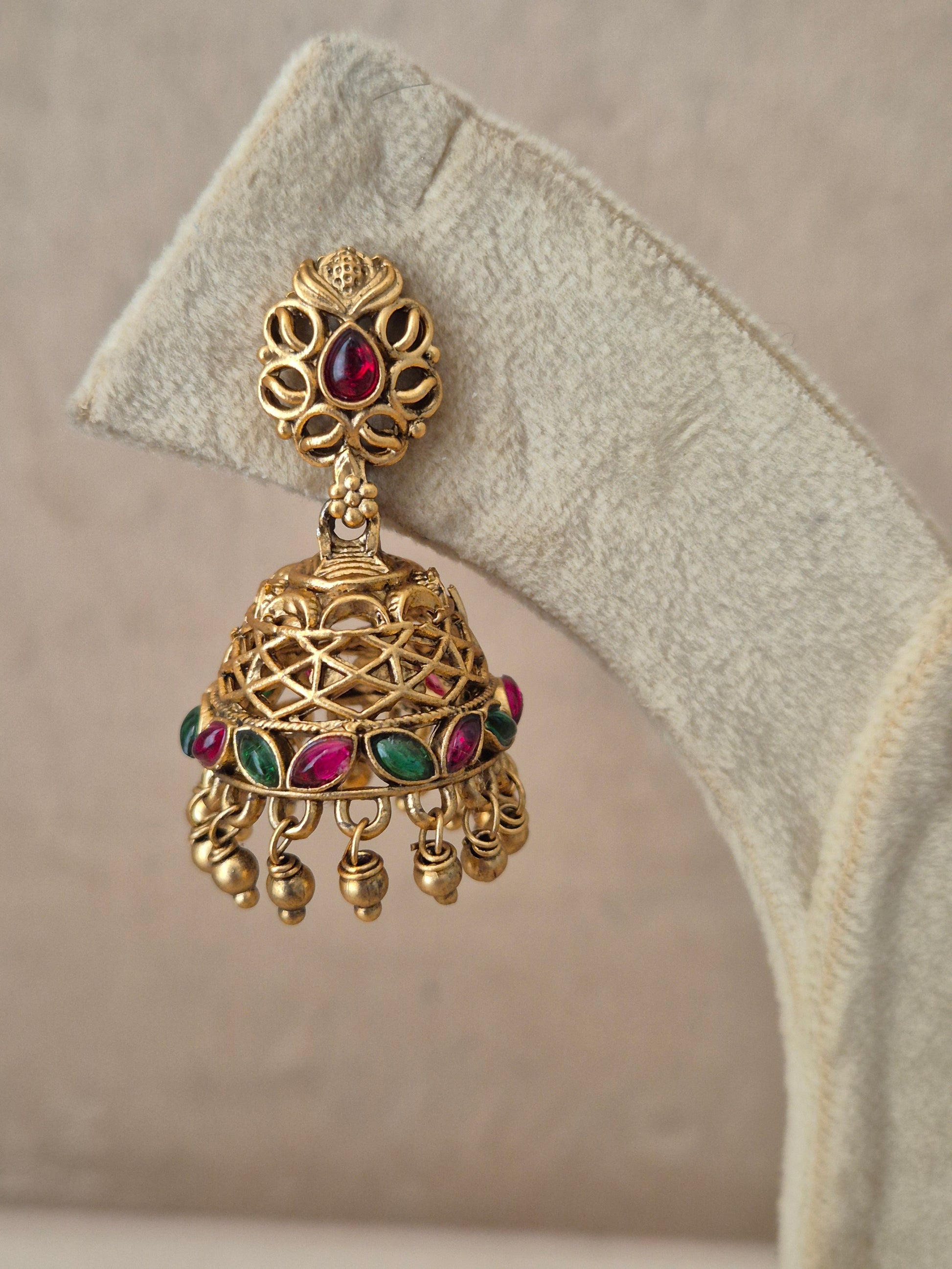 Close-up of Naitri Vedshri premium gold ethnic earrings showcasing traditional Indian temple jewelry craftsmanship with vibrant red and green gemstone accents and metallic bead fringe by naitri.in