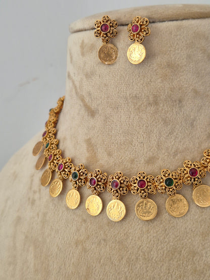 Gold coin necklace and matching stud earrings the necklace features gold coin-shaped charms interspersed with small red and green gemstone floral accents by naitri.in
