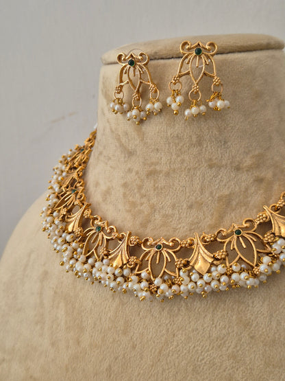 Gold-toned traditional jewelry set  featuring a pearl-embellished floral choker and matching dangling earrings with small green stone accents by naitri.in