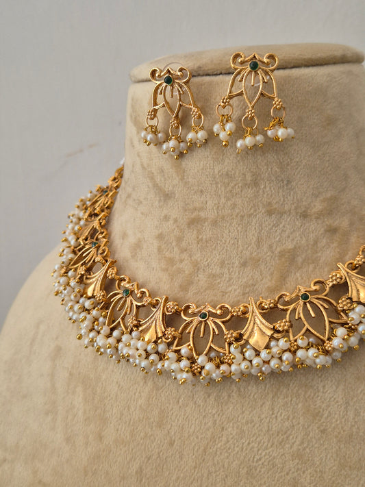 Gold-toned traditional jewelry set  featuring a pearl-embellished floral choker and matching dangling earrings with small green stone accents by naitri.in
