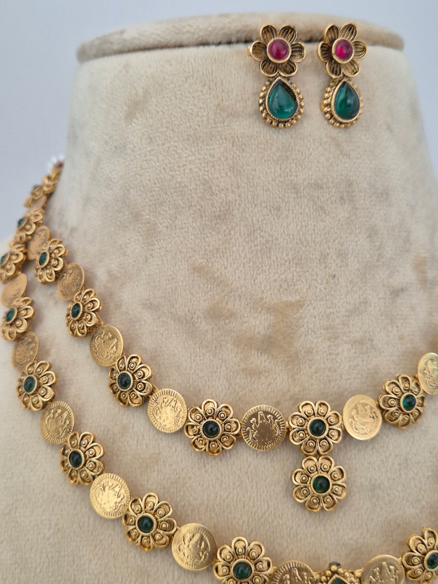 Gold-toned jewelry set featuring a necklace with coin-style links and floral motifs accented with green and dark green stones, plus matching earrings with pink and green teardrop stones by naitri.in