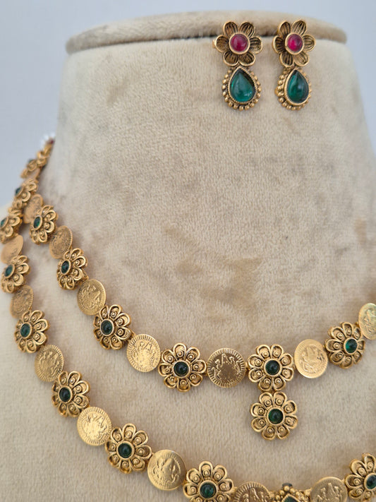 Gold-toned jewelry set featuring a necklace with coin-style links and floral motifs accented with green and dark green stones, plus matching earrings with pink and green teardrop stones by naitri.in