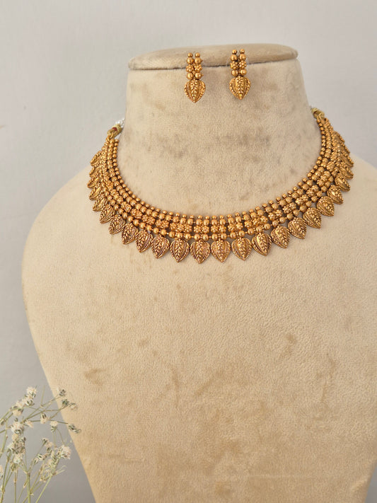 Gold-toned traditional necklace and matching drop earrings Traditional gold-toned choker necklace and drop earrings set with detailed metallic leaf drops and textured bead patterns by naitri.in