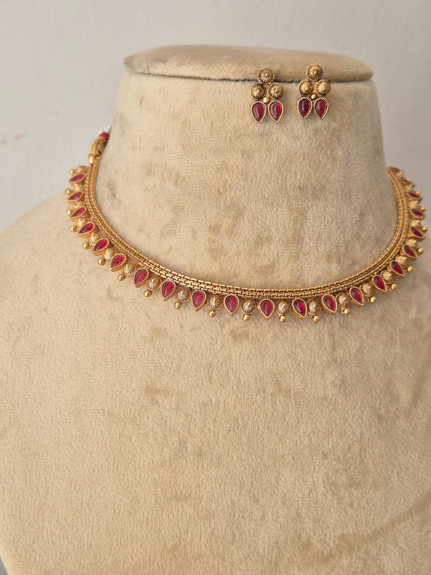 Gold-toned traditional Indian jewelry set featuring a choker necklace and matching earrings, embellished with red teardrop-shaped stones, By naitri.in