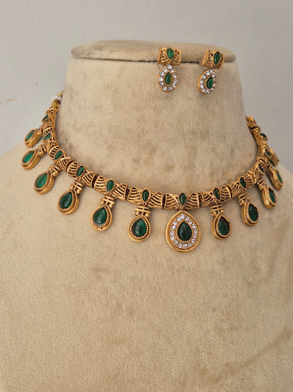 Gold-toned traditional jewelry set including a necklace and matching earrings, decorated with green teardrop-shaped stones and small clear stones by naitri.in