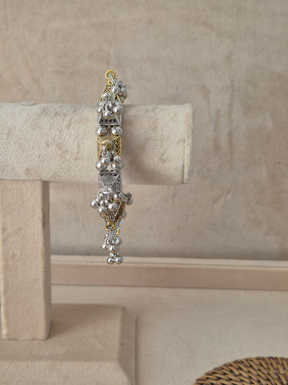 Dual-tone Yachana bangle bracelet featuring an alternating pattern of textured oxidized silver panels and gold-plated floral frames, finished with prominent clusters of dangling silver ghungroo charms,by naitri.in