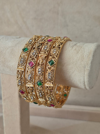Close-up of Naitri Yamini premium gold ethnic bangle set with traditional Indian filigree engraving and vibrant red and green stone accents by naitri.in