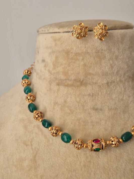 A traditional Indian necklace set with alternating green and gold beads, a central floral pendant with a red stone, and coordinating gold-toned floral studs by naitri.in