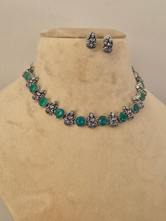 A silver-toned jewelry set featuring a necklace and matching earrings with small metallic motifs and round green stones by naitri