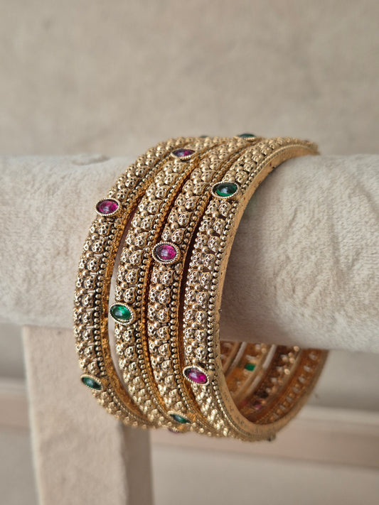 A stack of four gold-toned bangles adorned with clear stones and small green and pink gemstone accents, by naitri.in
