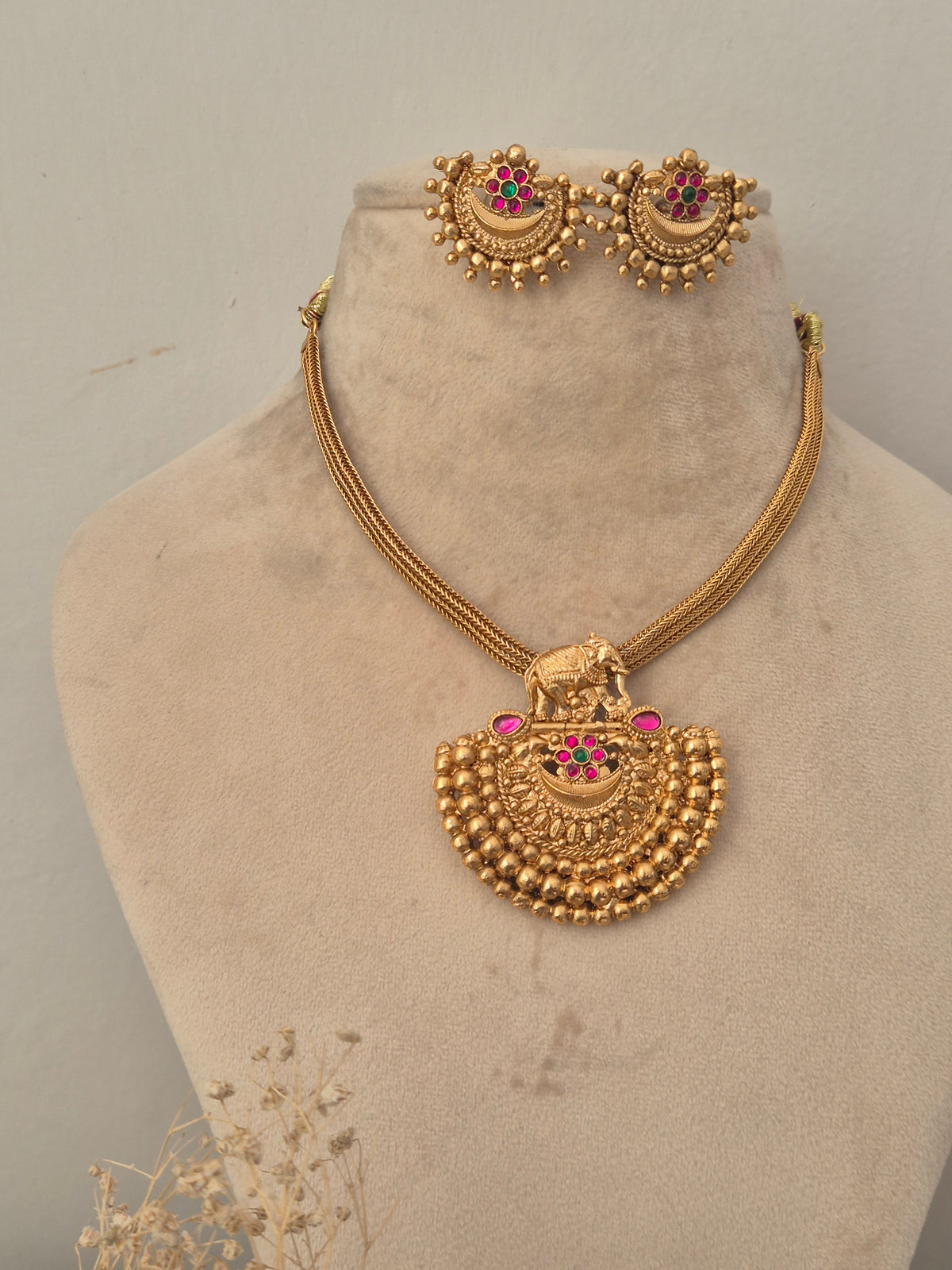 Gold temple necklace set with an elephant pendant, pink stone highlights, and matching stud earrings by naitri.in
