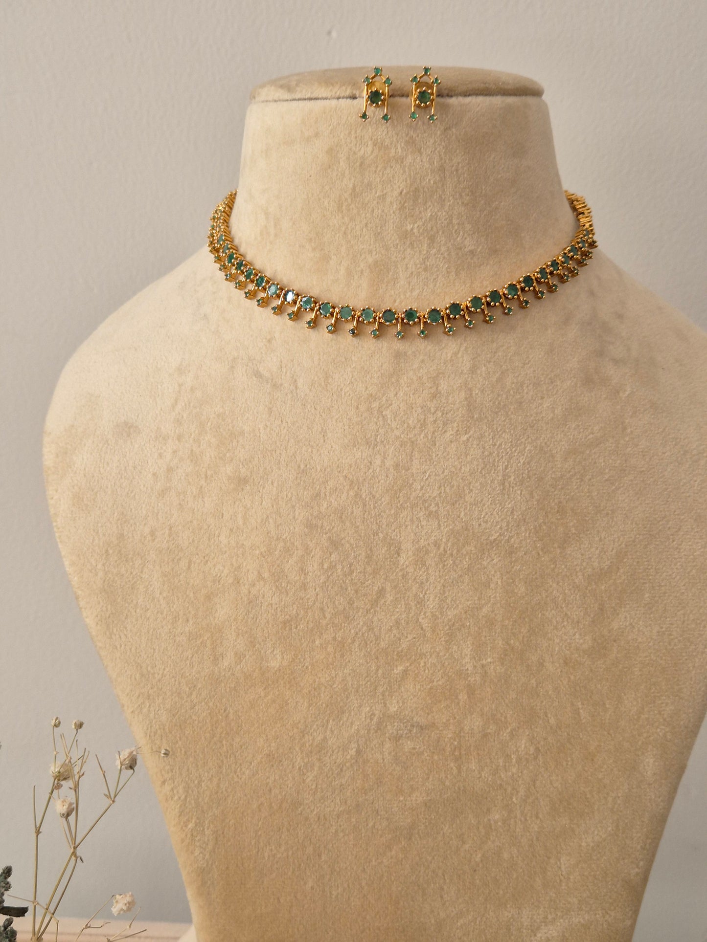 Set featuring a delicate gold-toned choker with alternating green gemstones and small golden beads, paired with matching green stone stud earrings by naitri.in