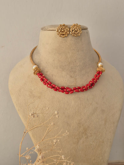 Handcrafted Golden Ethnic Necklace with bright red beaded strands styled on a display bust, accompanied by matching floral-textured gold-toned studs by Naitri.in