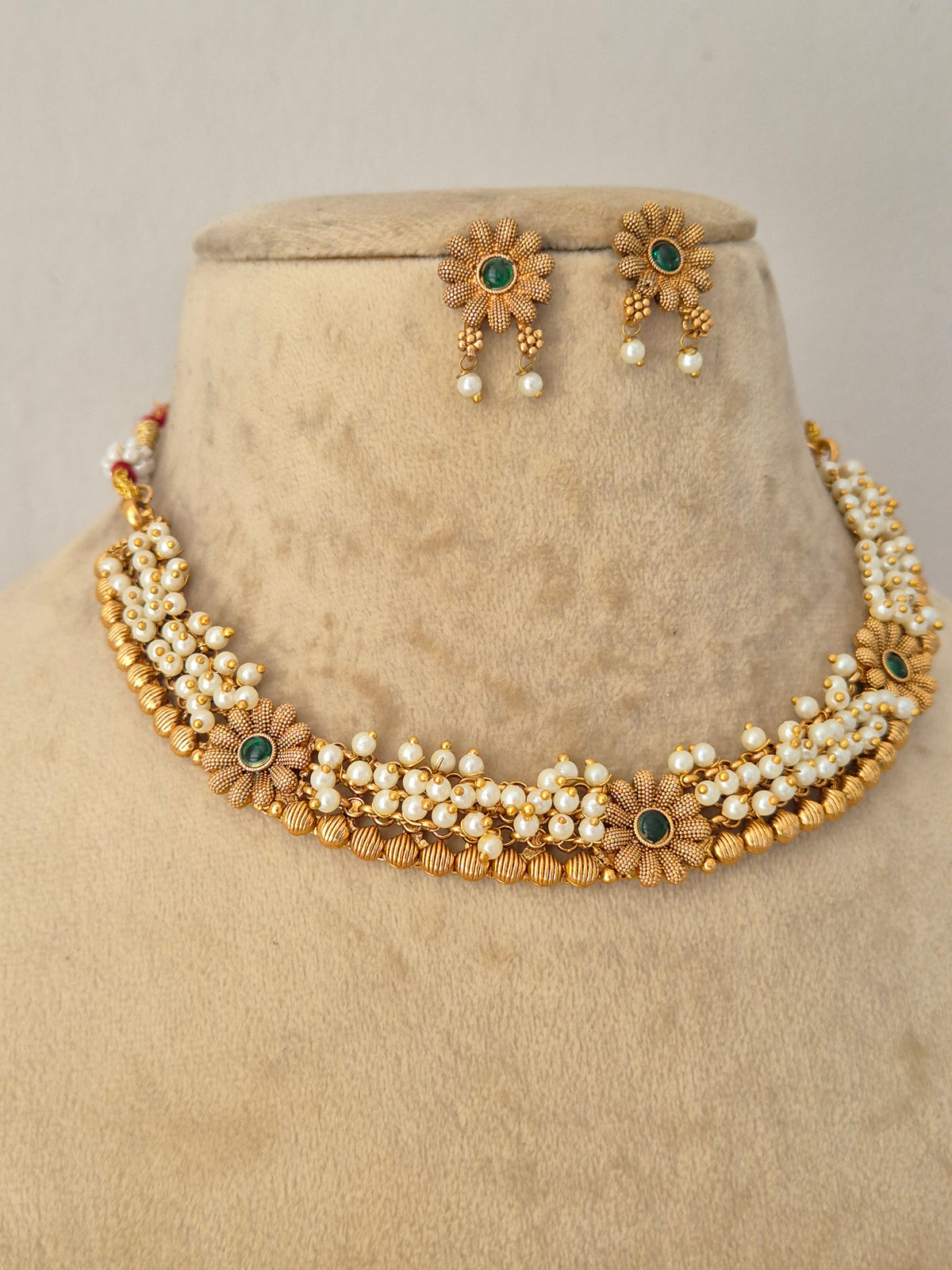 Anima pearl and gold choker necklace set with intricate gemstone detailing and matching floral stud earrings displayed on a beige mannequin Naitri.in