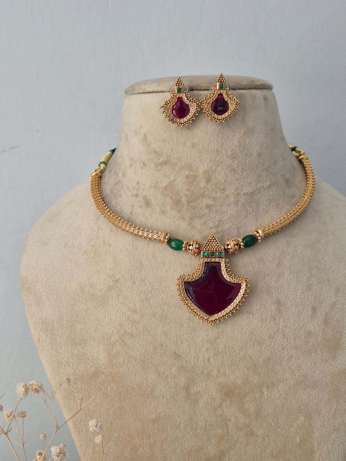 Traditional Indian gold-toned choker necklace set with a prominent red gemstone pendant and matching earrings by Naitri.in