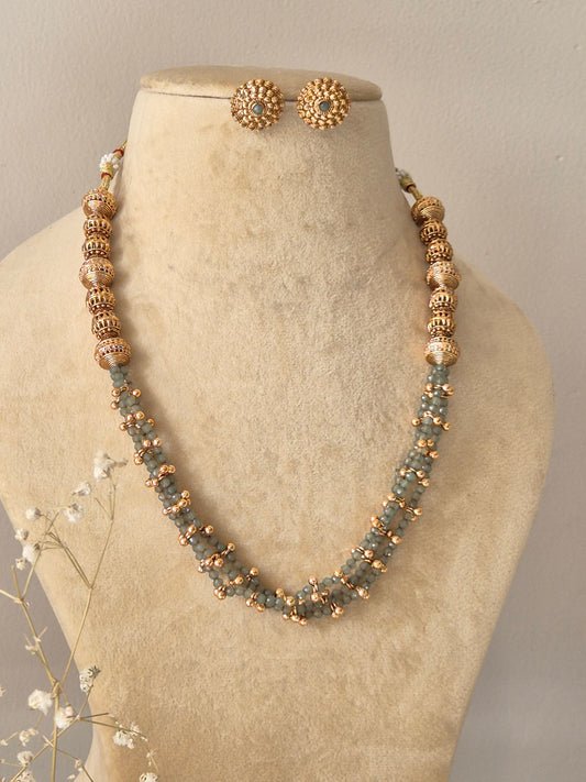 Elegant multi-layered beaded necklace in a golden finish with intricate metallic spacers and matching floral-patterned gold studs by naitri.in