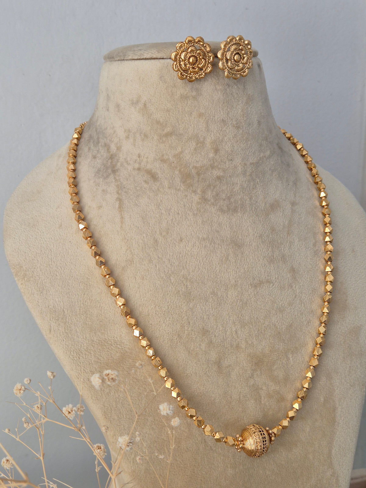 Handcrafted ethnic brass alloy necklace with a textured central pendant bead, faceted gold-toned beads, and matching stud earrings by Naitri.in