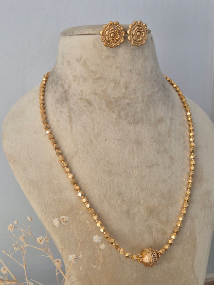 Handcrafted ethnic brass alloy necklace with a textured central pendant bead, faceted gold-toned beads, and matching stud earrings by Naitri.in